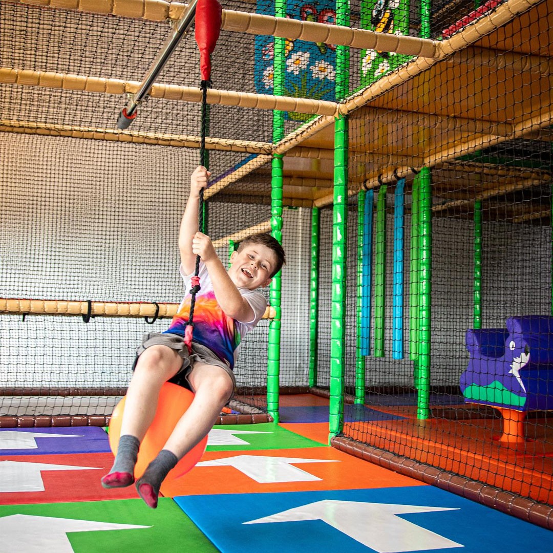 A young child enjoying themselves on a swing in an indoor soft play.